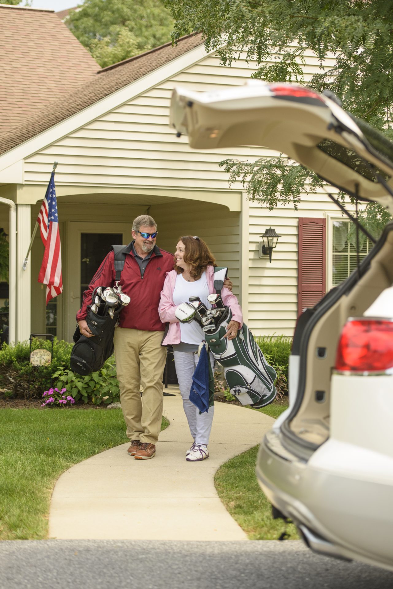 OIlder couple holding golf clubs and walking towards car with hatch open.
