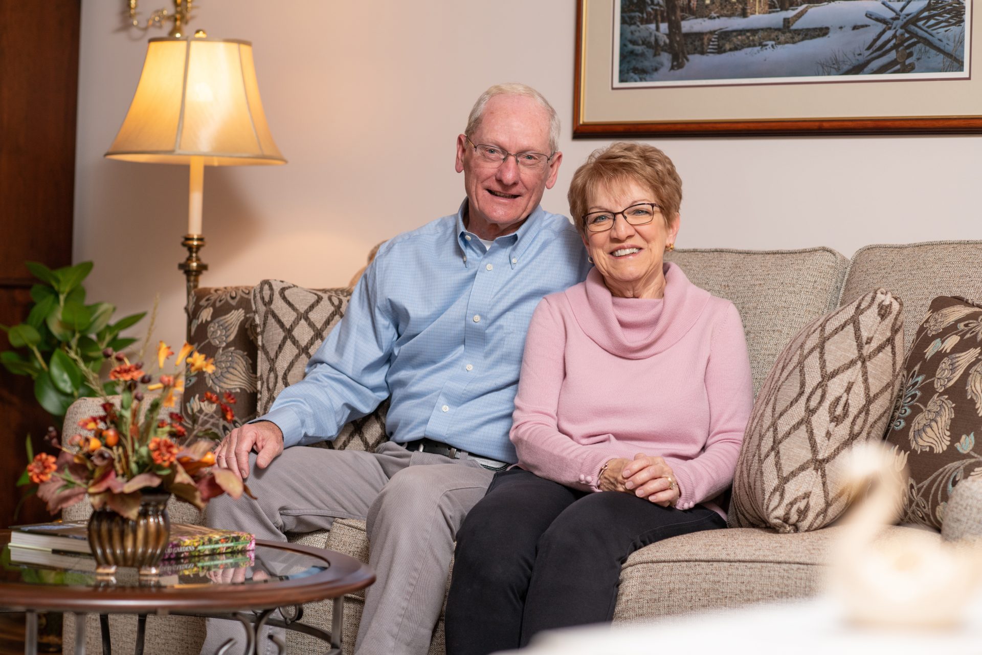 An elderly couple sitting on the couch smiling and looking at camera