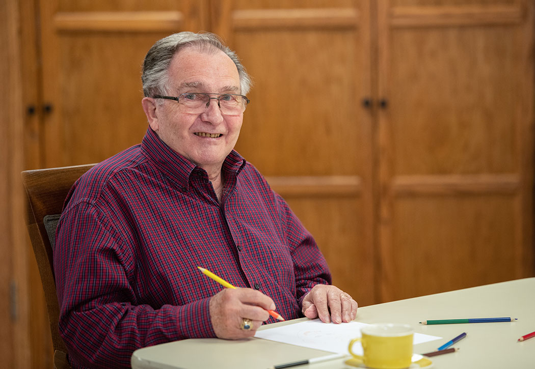 Elderly man drawing a picture and smiling at a table
