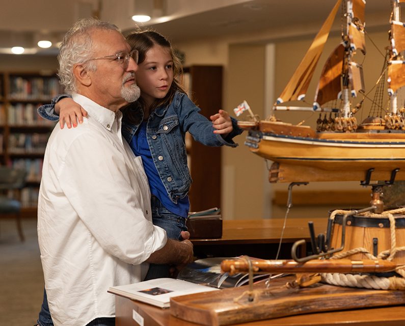 Young girl with her grandfather looking at a model replica of a ship