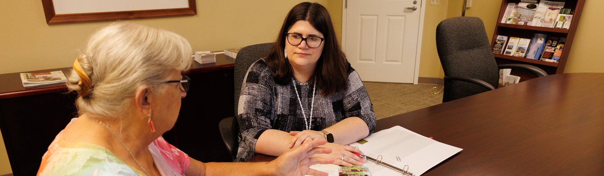 two women are sitting at a table looking at a binder