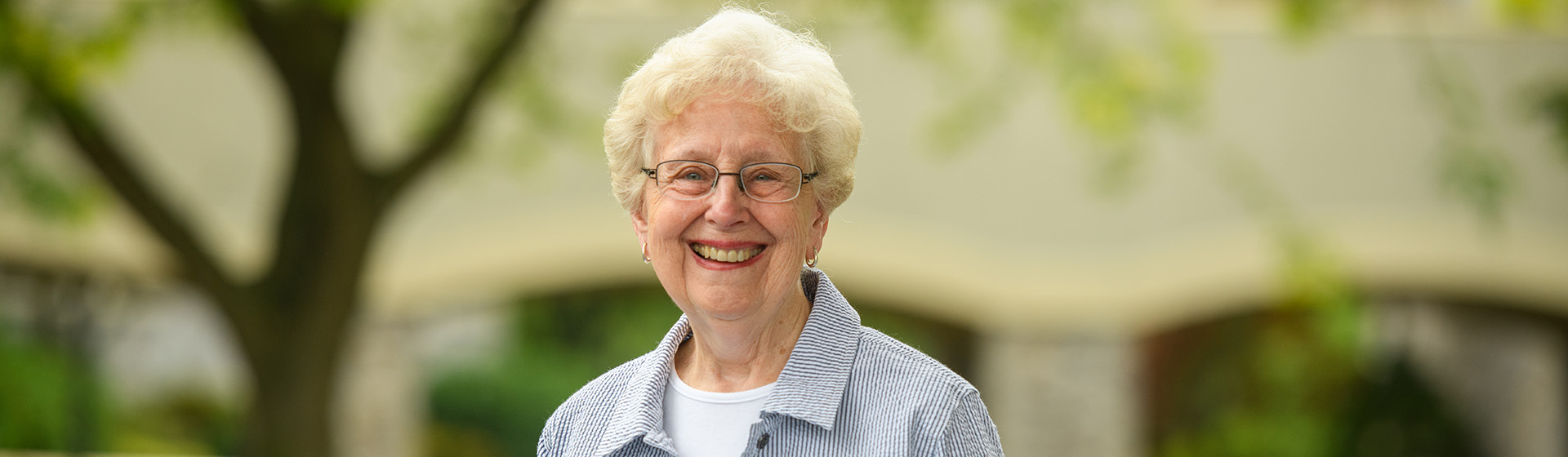 an older woman wearing glasses and a striped shirt smiles for the camera